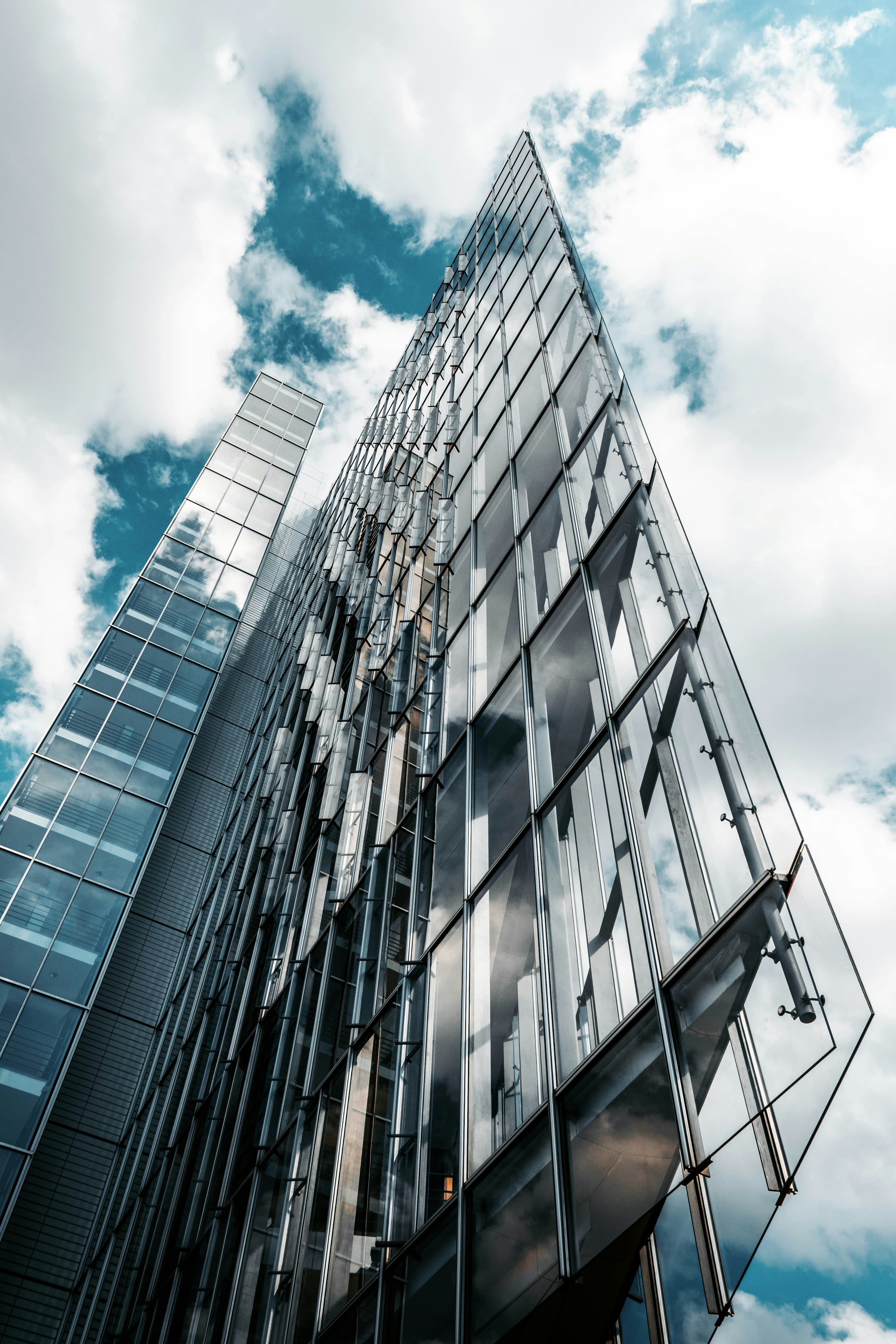 Tiefwinkel-Architekturfotografie eines modernen Glas-Wolkenkratzers vor bewölktem Himmel